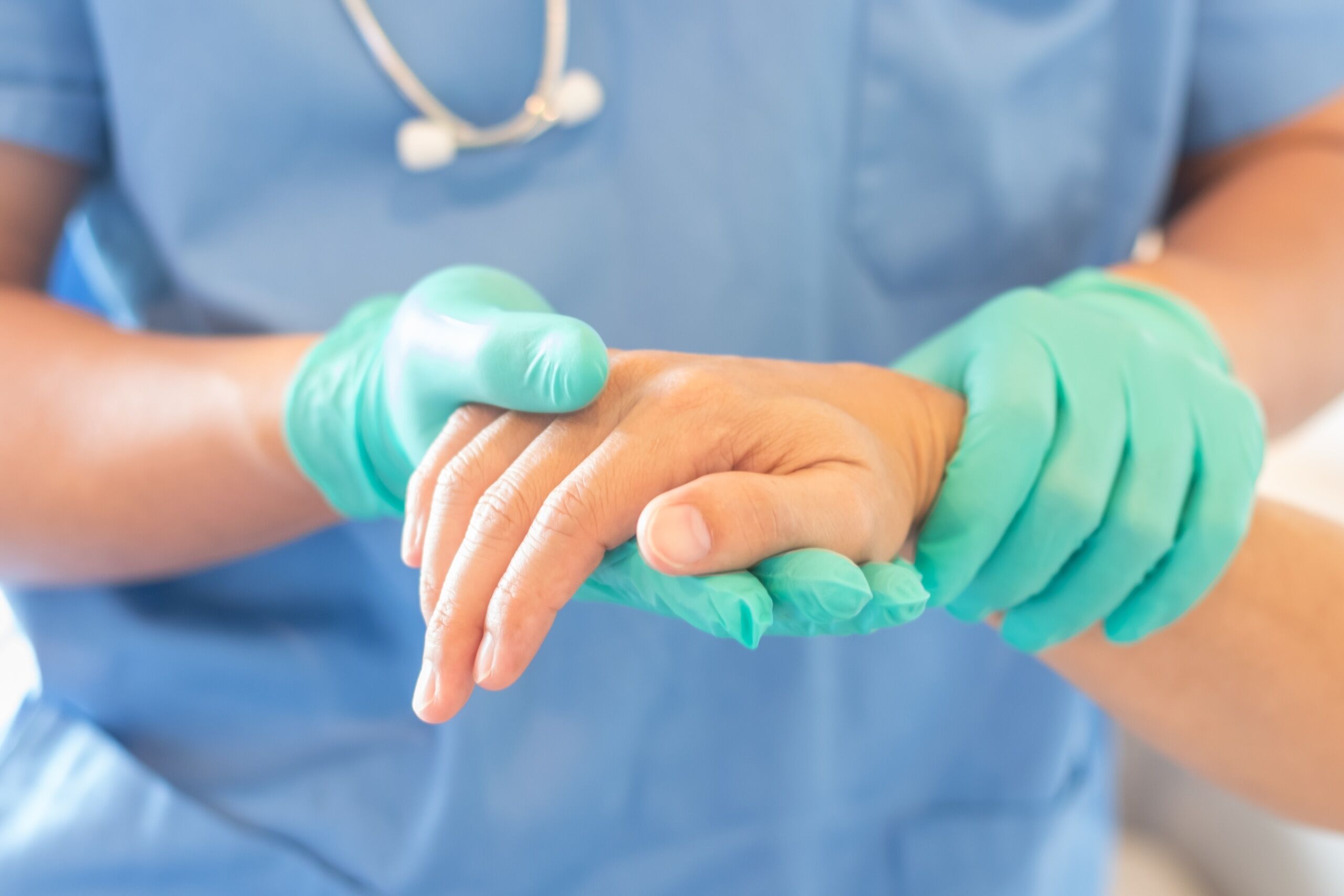 Close up of a medical professional wearing gloves and holding a patient's hand