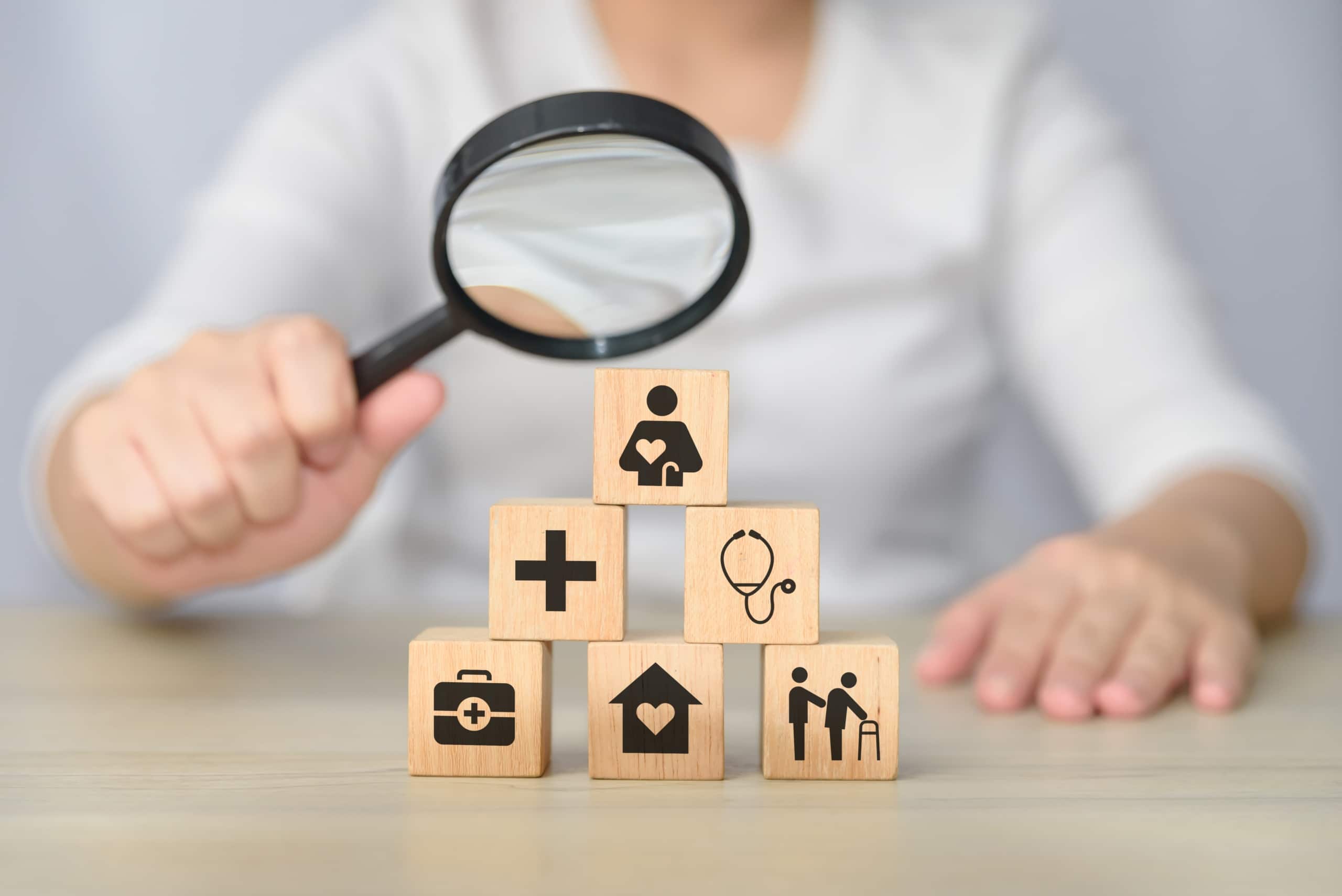 Woman using a magnifying glass over blocks with healthcare symbols