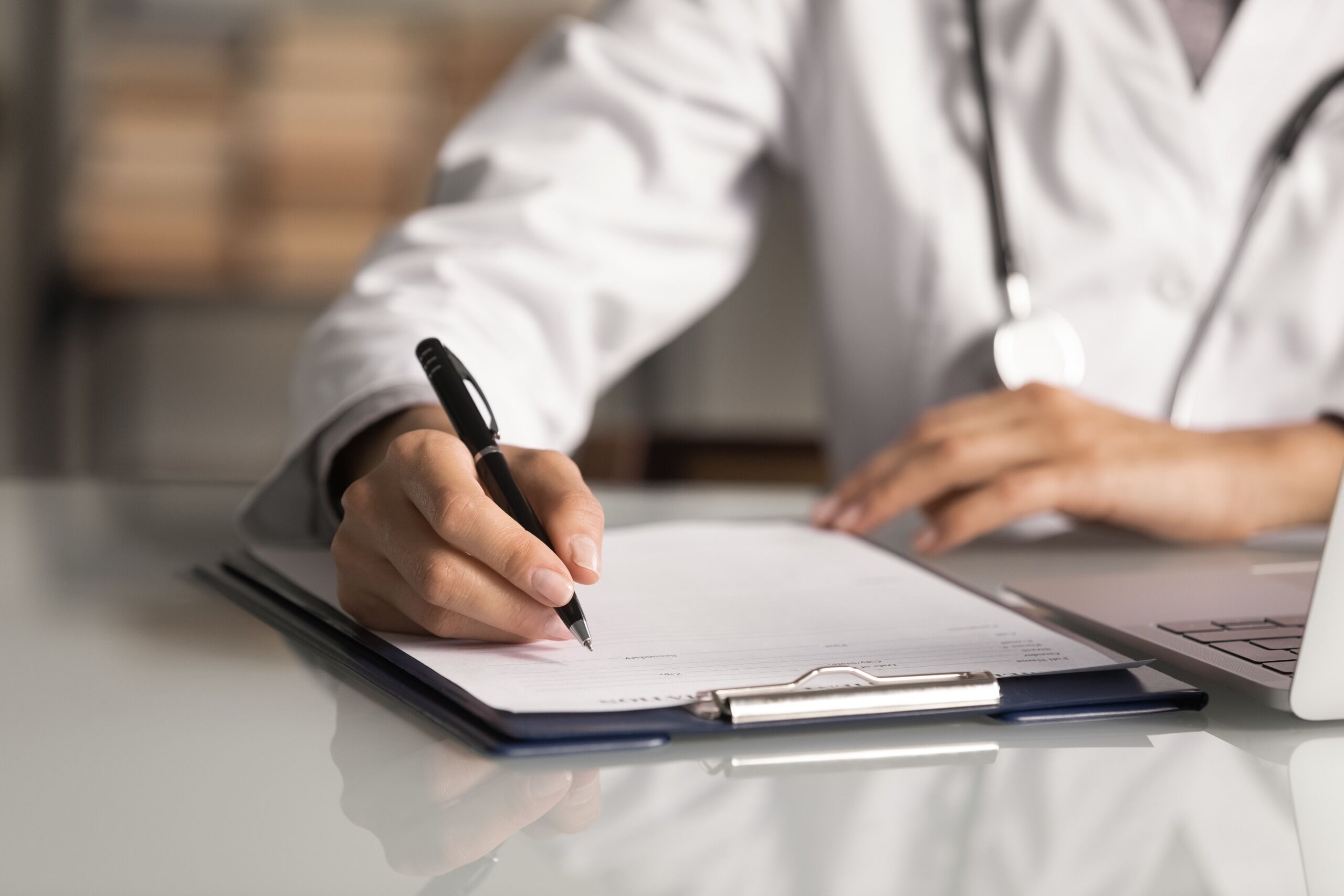 Close up of a medical professional writing on a clipboard