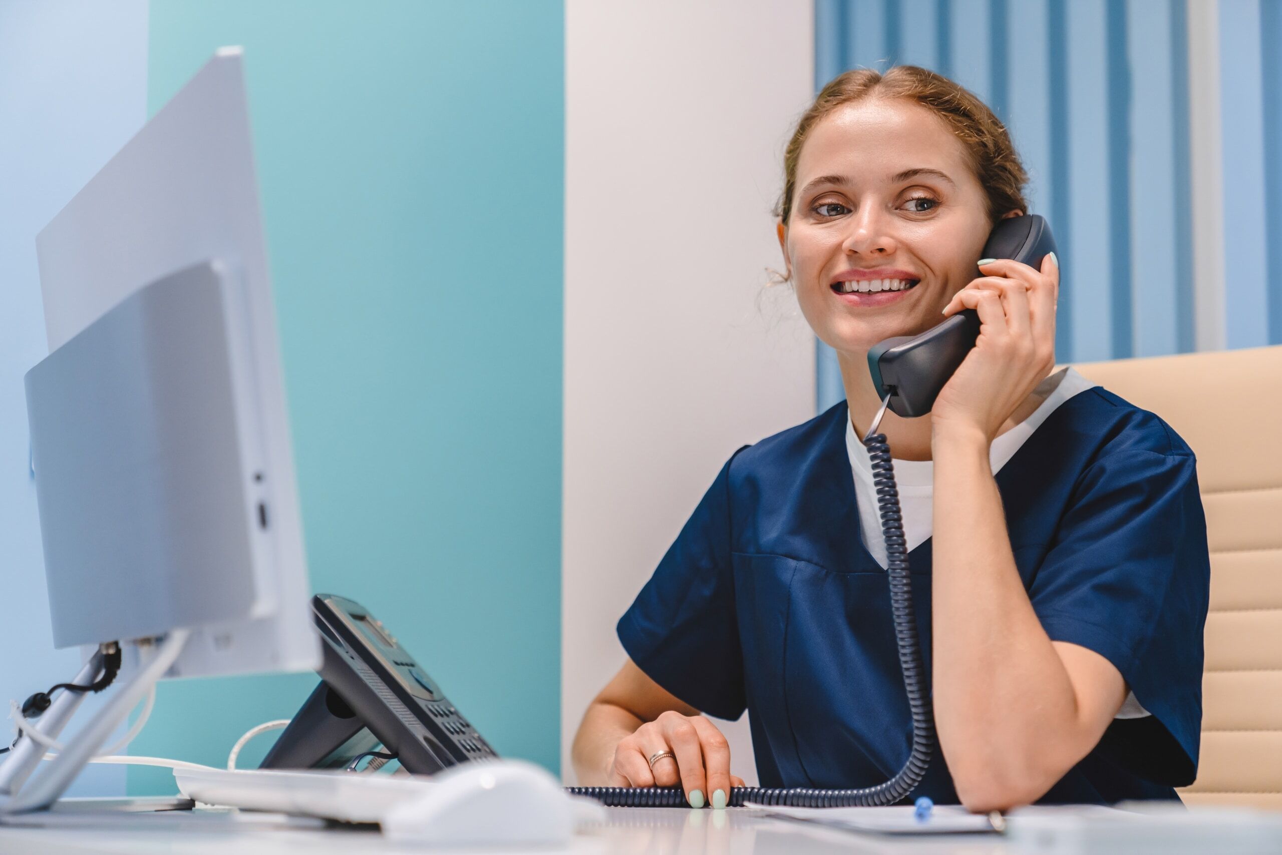 Medical professional in scrubs using a phone and computer